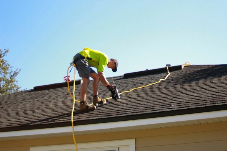 Homeowner in safety gear inspects a gutter from a stabilized ladder while holding gloves and a soft brush.